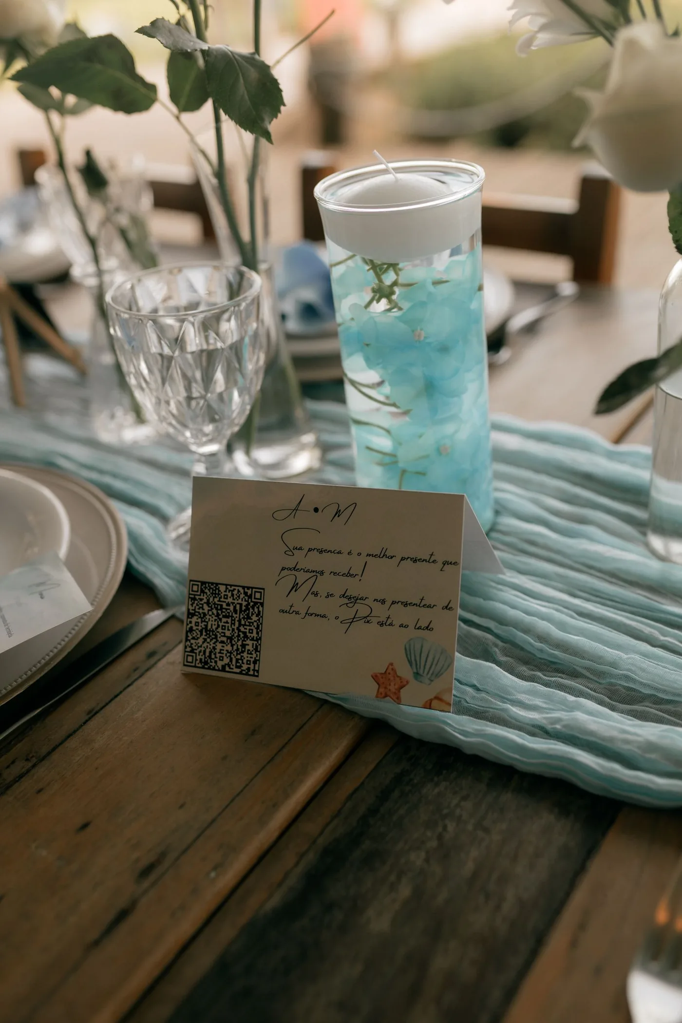 Une carte avec un QR code posée sur une table de mariage dressée, entre une bougie et des fleurs