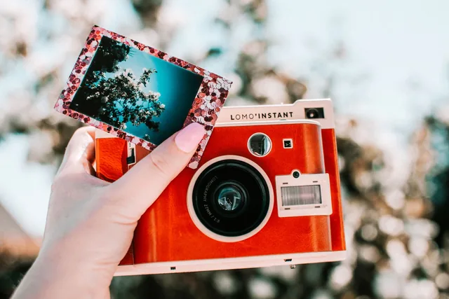 Une main tient un appareil photo instantané rouge avec une photo fraîchement développée